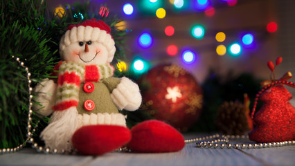 Obraz na płótnie Canvas Snowman sits on the table next to Christmas toys on the back of the bokeh