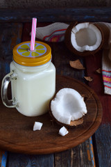 Coconut milk in bottle with broken coco on wooden background. Delicious milk cocktail. Copy space