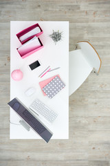 Stylish workplace of female employee: wooden desk with modern computer, smartphone and pink stationery, directly above view