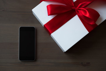 Black mobile phone and white gift box, decorated with a red satin bow on the table
