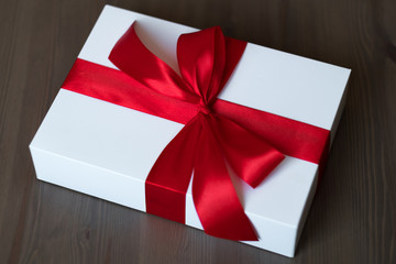 A white gift box decorated with a red satin bow on the table