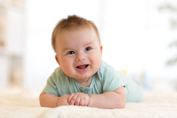 Very happy laughing baby in blue clothes lying on his belly.