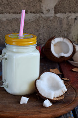 Coconut milk in bottle with broken coco on wooden background. Delicious milk cocktail. Copy space