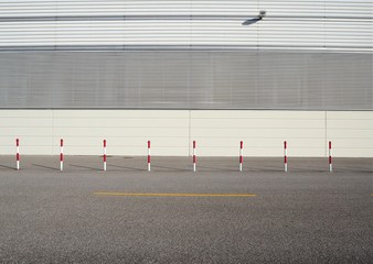 Urban street background. White and red poles on asphalt road in front of a white wall made of aluminium panels