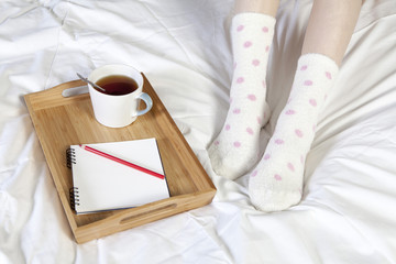 A tray with a cup of coffee, a notepad and a pencil stands on the bed