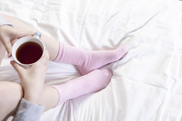 the Hands holding a cup of coffee. You can see the legs in pink socks.
