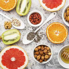 Ingredients of healthy dietary food breakfast pink grapefruit, orange, chia seeds, quinoa, green herbs, kiwi, wild rice, almonds, walnuts, hazelnuts on a light marble background. The concept of