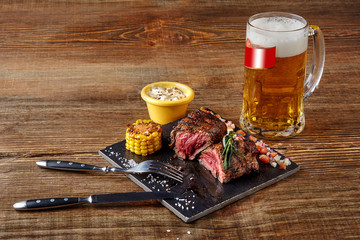 Grilled tenderloin Steak roastbeef and mushrooms sauce on black cutting board and glass of beer on wooden background