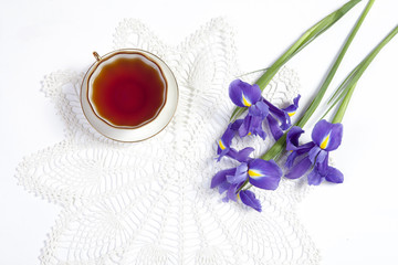 Obraz na płótnie Canvas Violet Irises xiphium (Bulbous iris, sibirica) with cup of tea on white background with space for text. Top view, flat . Holiday greeting card for Valentine's Day, Woman's Day, Mother's Day, Easter!