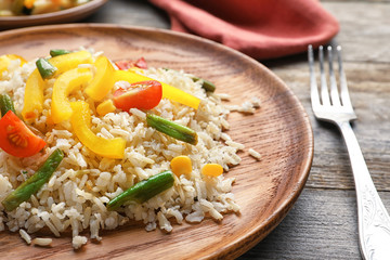 Wooden plate of tasty brown rice with vegetables on table, closeup