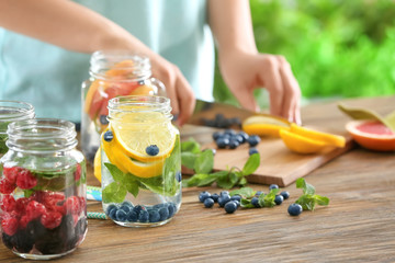 Blurred view of woman preparing infused water with fruits and berries in mason jar - obrazy, fototapety, plakaty