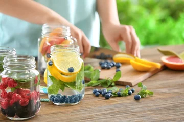 Wall murals Water Blurred view of woman preparing infused water with fruits and berries in mason jar