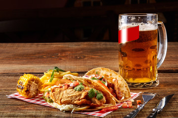 First corn tortilla with grilled chicken fillet, second with fish fillet, sauce and beer on wooden table