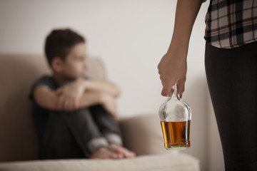 Woman holding bottle of alcohol and blurred little boy on background