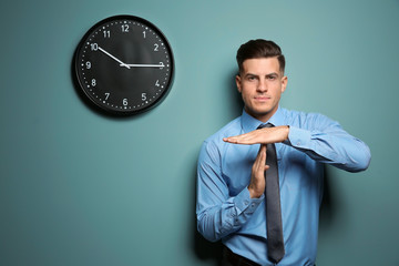 Handsome manager showing time out gesture near color wall with clock
