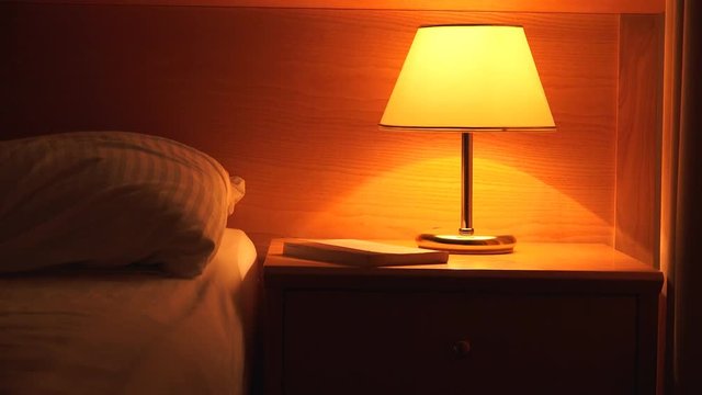 Book and vintage lamp on night table in hotel room. Retro styled bedroom interior.