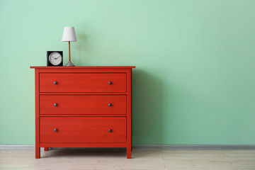 Red chest of drawers with clock and lamp near color wall
