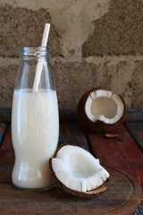 Coconut milk in bottle with broken coco on wooden background. Delicious milk cocktail. Copy space