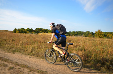 Naklejka premium Male cyclist with backpack driving by rural dirt road outdoors