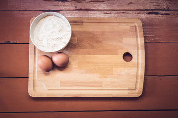 Flour, eggs and cutting board on rustic painted wooden background. Top view with copy space