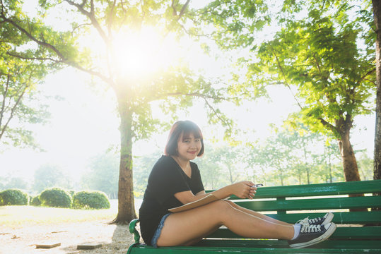 Happy hipster young asian woman writing into her diary in park. Happy hipster young asian woman working on notebook in park. Student studying outdoors. Lifestyle woman outdoor concept. Flare light.