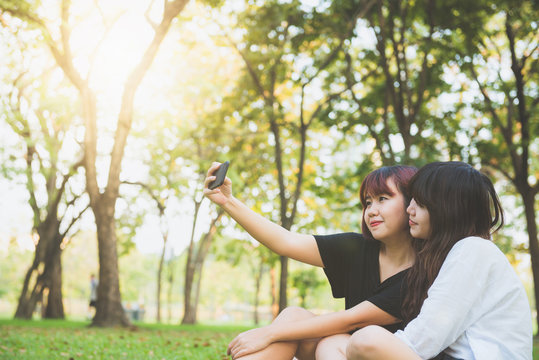 Two beautiful happy young asian women friends having fun together at park and taking a selfie. Happy hipster young asian girls smiling and looking at smartphone. Lifestyle and friendship concepts.
