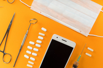 on an orange background is a smartphone, dental instruments and pills