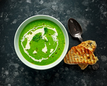 Green sweet pea and mint soup with cream and olive oil drizzle served with grilled ciabatta toasts