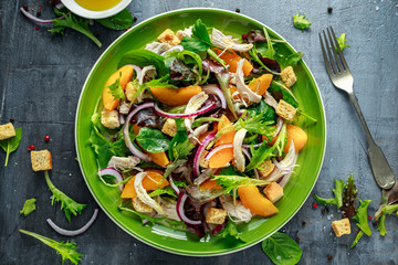 Fresh salad with chicken breast, peach, red onion, croutons and vegetables in a green plate. healthy food