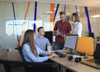 Group of young modern people in smart casual wear having a brainstorm meeting while standing in the creative office.