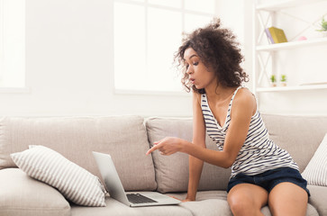 Obraz na płótnie Canvas Shocked girl with laptop sitting on beige couch