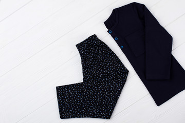 Dark pajama set on white. Floral pants and navy t-shirt with blue buttons. Folded clothes on wooden rack at the shop.