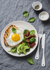 Morning breakfast table. Fried egg grilled sandwich and spinach, tomato, avocado salad on a gray background, top view