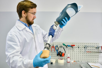 Portrait of young  prosthetics technician holding prosthetic leg  checking it for quality and...