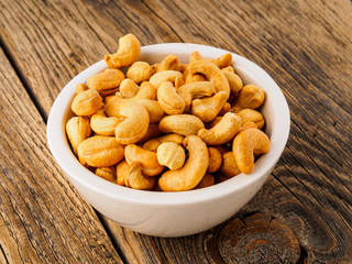 Cashew nuts in  white cup on brown wooden background, side view.