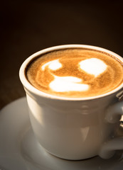 A cup of coffee with valentine milk foam on the white plate and wooden table.