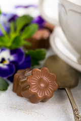Chocolate candies in flower shape with violets and cup of coffee. Holiday food concept with copy space.