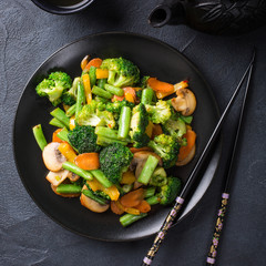 Hot stir fried vegetables on black plate. Healthy asian food concept with copy space.