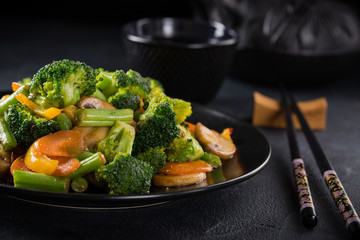 Hot stir fried vegetables on black plate. Healthy asian food concept with copy space.