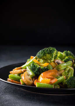 Hot stir fried vegetables on black plate. Healthy asian food concept with copy space.