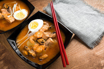 Soup with shrimps in bowl with tomatoes and herbs on wooden table.