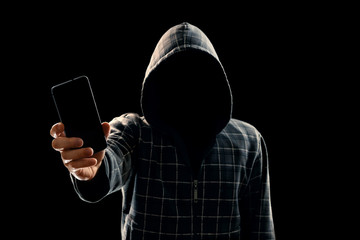 Silhouette of a man in a hood on a black background, his face is not visible, the hacker is holding...
