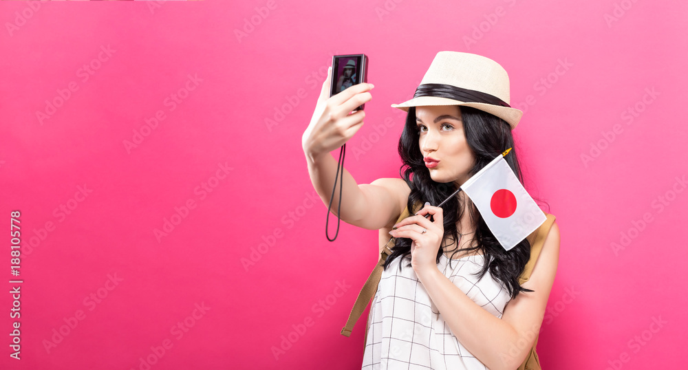 Wall mural traveling young woman holding a camera with japanese flag on a solid background