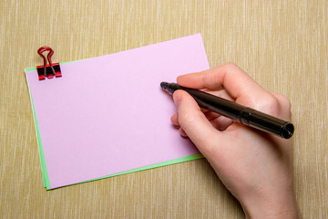 pink paper with paperclip and woman hand holding a pen about to write. Objects isolated on yellow