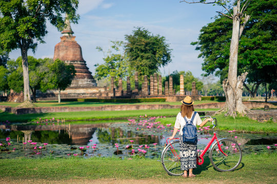 Young woman traveler travelling by bicycle into Wat Mahathat temple in the Sukhothai Historical Park contains the ruins of old Sukhothai, Thailand, UNESCO world Heritage Site.