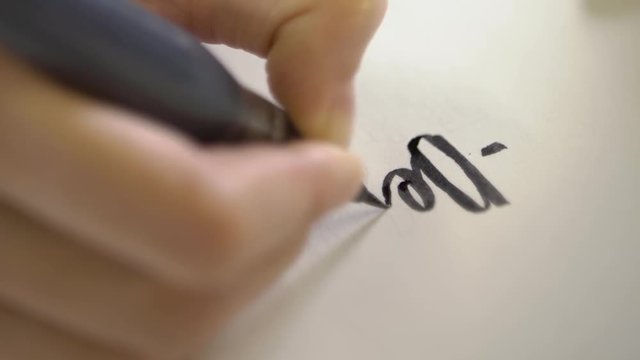 A close-up of a brush drawing calligraphic letters on paper.