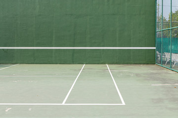 Outdoor tennis court and green knock board with white lines for personal practice.