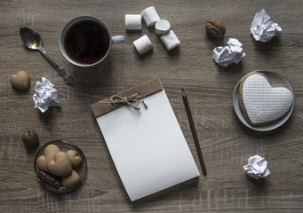on a wooden background lies a craft notepad scrapbooking plate cookie heart pencil brown mug coffee marshmallow nuts lump paper mint spoon 