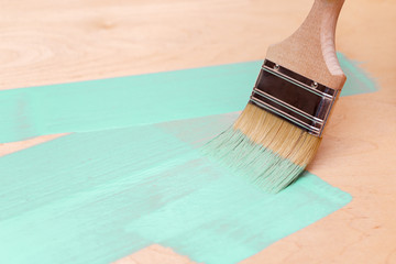 Staining the wooden surface of turquoise paint using a paint brush