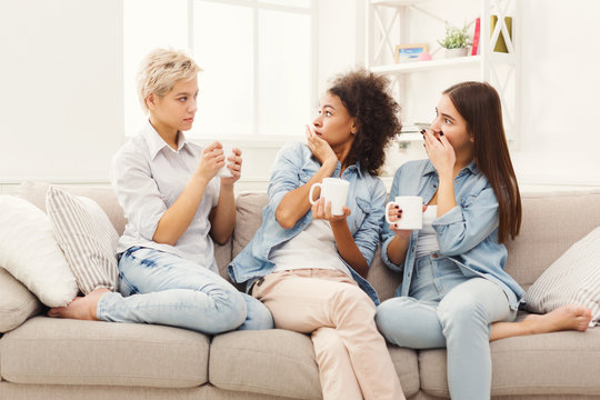 Three young female friends with coffee chatting at home